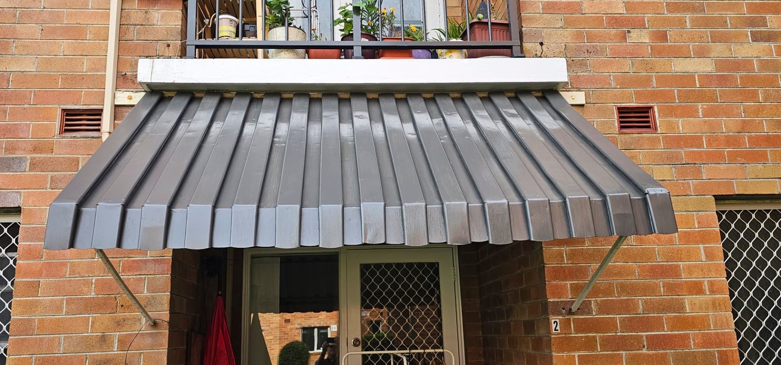 Metal entry awning repainted in charcoal against a brick wall